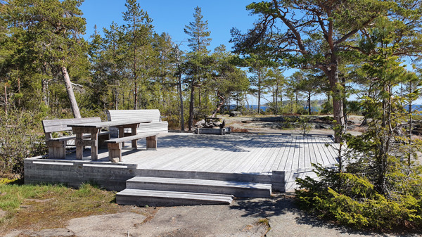 Eldstad och bänkar sedd nedifrån. Trädäck och rullstolsanpassad stig finns hela vägen från parkering.