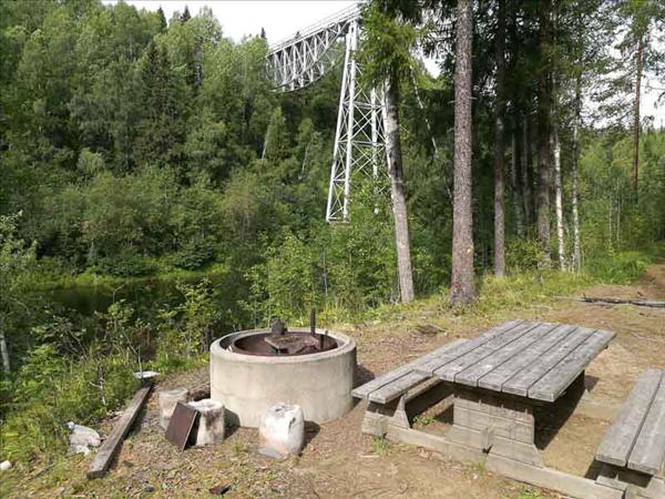 Eldstad med picknickbord intill. Den äldsta bron i bakgrunden